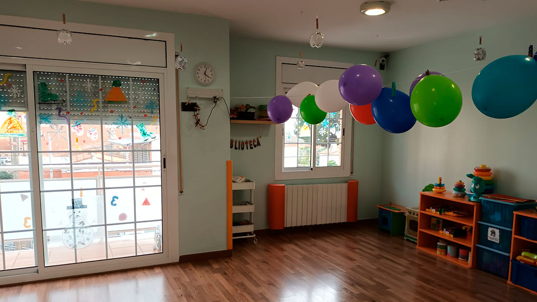 Imagen de una aula luminosa para niños de 12 a 24 meses con juguetes y globos decorativos.